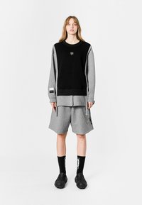 Sudadera negra y gris, pantalones cortos grises holgados, calcetines negros con texto blanco y zapatos negros texturizados. Presenta un diseño en capas y una marca sutil.