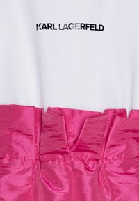 White top with black "KARL LAGERFELD" logo; pink satin ruffled fabric at the bottom, featuring a smooth texture and layered design.
