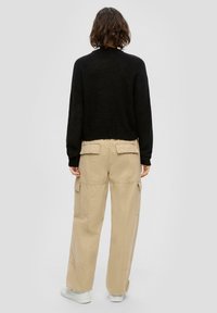 Schwarzer, taillierter Strickpullover mit gerippter Textur, kombiniert mit beigen Cargo-Hosen mit seitlichen Taschen und einer lockeren Passform. Weiße Sneaker inklusive.