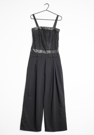 Mono negro sin mangas con cuerpo de encaje, ribete de cuero sintético, pantalones de pierna ancha y bolsillos delanteros con solapa y botones en la cintura, colgado en una percha negra.