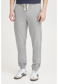 Grå sweatpants lavet af blødt stof med ribbede manchetter, elastisk talje og kontrasterende snore. Kombineret med hvide og grå sneakers.