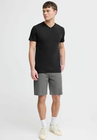 Svart V-hals t-skjorte med korte ermer, sammen med grå shorts. Modellen har på seg hvite sokker og lyse sneakers. Enkelt design.