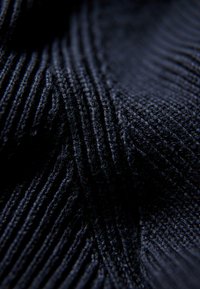 Dunkelblauer gestrickter Stoff mit strukturierter Rippoptik, der feine und grobe Linien enthält, die miteinander verwoben sind und Tiefe und Dimension erzeugen.