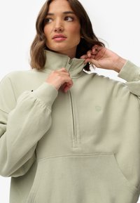 Lys grøn zip-up sweatshirt med høj krave, ribstrikkede manchetter, kengurulomme og broderet logo. Blødt stof med en afslappet pasform.