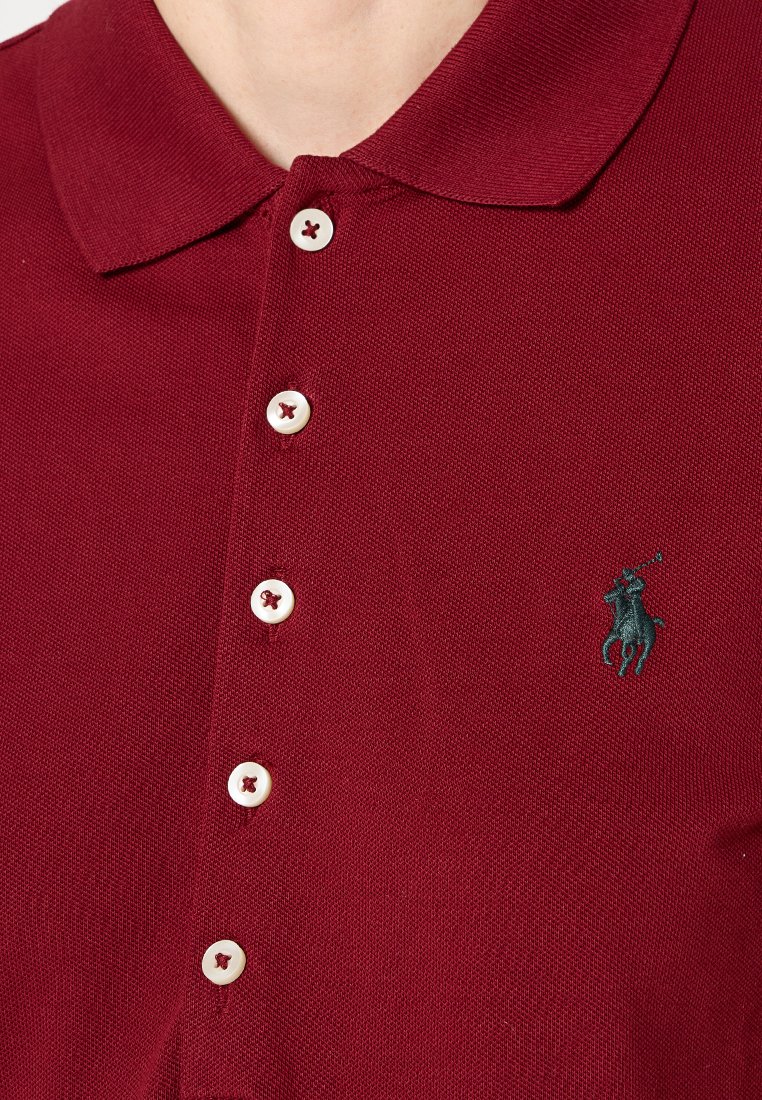 Bordowy polo z teksturowanej tkaniny, z kołnierzykiem, pięcioma białymi guzikami oraz zielonym haftowanym logo po lewej stronie.