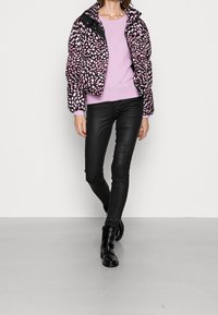 Giacca a vento con un motivo astratto nero e rosa, abbinata a un maglione di maglia rosa chiaro e pantaloni skinny in pelle nera, completata da stivali neri.