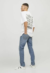 Camiseta blanca de gran tamaño con un diseño gráfico en la parte trasera, combinada con unos jeans de mezclilla azul claro y zapatillas blancas con detalles en negro.