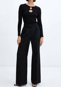 Czarny longsleeve z wycięciem w kształcie klucza przy dekolcie, zestawiony z czarnymi spodniami o szerokich nogawkach z wysokim stanem. Gładka faktura na całej powierzchni.