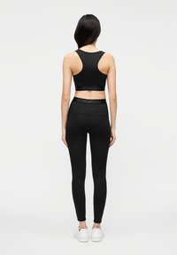 Sujetador deportivo negro con una banda ancha y diseño de espalda cruzada, combinado con leggings negros que cuentan con una pretina similar, ambos con una textura suave.