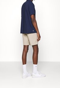 Marinblå kortärmad skjorta, beige shorts, vita sneakers och strumpor. Rak passform med en logo på skjortan och skorna. Slen tygtextur.