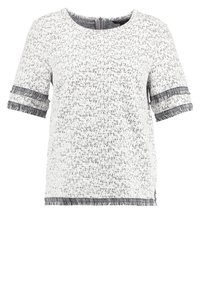 Haut blanc à manches courtes avec un motif texturé et des accents en franges aux poignets. Encolure ronde et coupe décontractée.