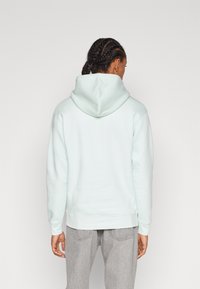 Ljusblå hoodie med en stor bakficka och huva med dragsko, gjord av mjukt, texturerat tyg, kombinerad med grå byxor.