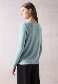 Hellblauer gestrickter Pullover mit langen Ärmeln und rundem Halsausschnitt, der über eine subtile Textur und einen lockeren Schnitt verfügt, kombiniert mit schwarzen Hosen.