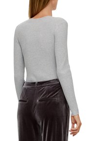 Grauer ribbeliger Langarm-Top mit taillierter Passform, kombiniert mit dunklen Samthosen mit Gesäßtaschen und glatter Textur.
