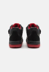 Černé vysoké tenisky s semišovým a syntetickým materiálem, červenými akcenty a nastavitelnými popruhy. Logo viditelné na patě.