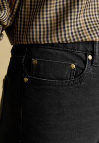 Čierne riflové nohavice so zlatými akcentmi, s predným vreckom a textúrovanou látkou. Kombinované s károvanou košeľou s vzorom.