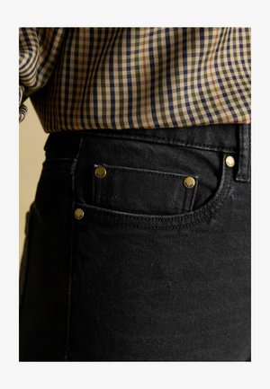 Black denim jeans with gold accents, featuring a front pocket and a textured fabric. Paired with a patterned, checkered shirt.