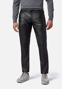 Zwarte leren broek met een slim fit ontwerp, gekenmerkt door een gladde textuur en zichtbare stiksels. Gecombineerd met grijze sneakers, wat een casual uitstraling geeft.