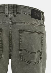 Harmaat denimfarkut, joissa on perinteinen taskumalli, takana logolappu ja näkyvät sauman yksityiskohdat. Pinta näyttää kuluneelta ja haalistuneelta.