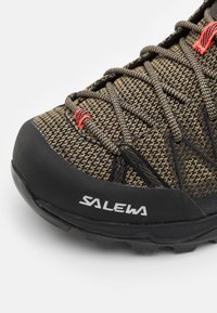 Struktureret brun og sort vandresko med gummitå, grå snørebånd og røde detaljer. "SALEWA" logo på siden.