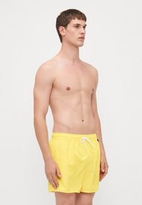 Gule svømmedrakt laget av lett stoff, med elastisk midjebånd med snøring og en sidelomme.