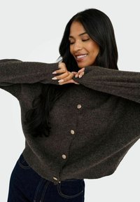 Brauner, lockerer Strickcardigan mit langen Ärmeln und sechs hellen Knöpfen auf der Vorderseite. Weiche Textur, lässiges Design.