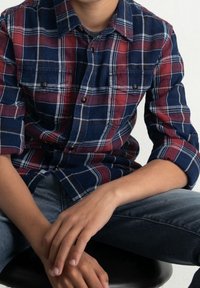 Chemise en flanelle à carreaux marine et bordeaux, avec un col boutonné, des manches longues retroussées et deux poches poitrine. Texture douce.