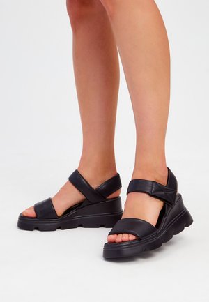 Sandalias de plataforma de cuero negro con dos correas entrelazadas y una correa ancha en la parte del dedo del pie. Suela texturizada con diseño de tacón en cuña.