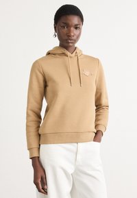Felpa marrone in tessuto morbido con tasca a marsupio, cappuccio con coulisse e polsini a costine. Ricamo del logo discreto sul petto.