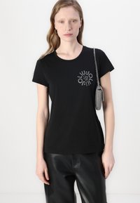 T-shirt nera a maniche corte in cotone con scollatura rotonda, caratterizzata da un design grafico circolare in argento sul lato sinistro anteriore.