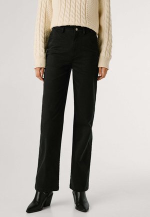 Pantalones negros de pierna ancha hechos de un tejido texturizado, con una cintura alta, bolsillos delanteros y un cierre de botón, combinados con zapatos negros de tacón.
