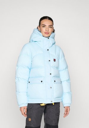 Lichtblauwe pufferjack met een hoge kraag, voorzien van een logopatch, drukknoopsluitingen en twee grote voorzakken. Zachte, gequiltte textuur.