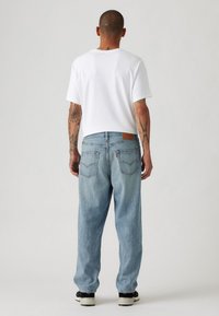 Lichtblauwe denim jeans met een relaxte pasvorm, vijf zakken ontwerp en een bruine leren patch op de achterkant van de tailleband. Witte t-shirt gedragen.