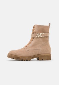 Botte de cheville en daim beige avec des lacets superposés, détail en métal doré avec le logo "MC", et une semelle crantée pour l'adhérence.