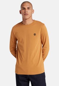 Langarmshirt in oranje-bruin katoen met een ronde halslijn en een klein zwart boomlogo op de borst; eenvoudig ontwerp zonder patronen.