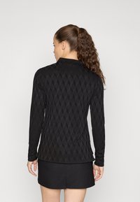 Čierny top s dlhým rukávom so štruktúrovaným diamantovým vzorom, s golierom a priliehavým strihom, v kombinácii s čiernou sukňou.