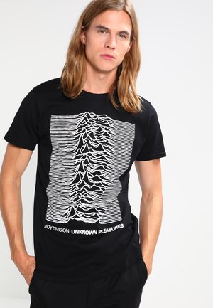 T-shirt en coton noir avec un design de lignes horizontales blanches ressemblant à des ondes sonores, avec le texte "JOY DIVISION - UNKNOWN PLEASURES" en bas.