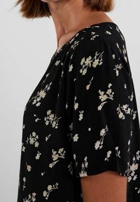 Černý top s krátkým rukávem, zdobený květinovým potiskem v krémových a světle zelených tónech. Měkká tkanina, volný střih s kulatým výstřihem.