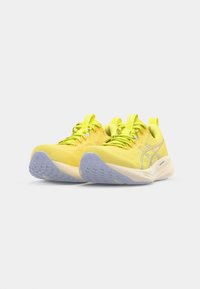 Chaussures de sport jaunes avec tige en maille, bout rond, semelle en caoutchouc violet et grip texturé. Présente des lacets contrastants et des languettes au niveau de la cheville.