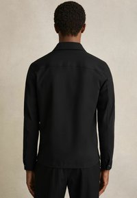 Zwarte langpols shirt met een klassieke kraag, gladde textuur en knoopmanchetten. Heeft een rechte snit en een minimalistisch ontwerp.
