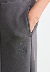 Main dans une poche avant de pantalon The North Face gris foncé, en tissu texturé, sur un fond clair.