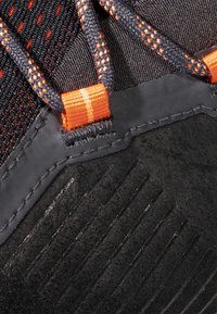 Scarpa sportiva nera con tomaia in materiale mesh e accenti arancioni, dettagli testurizzati e sovrapposizioni in gomma nera dal design elegante e a contrasto.