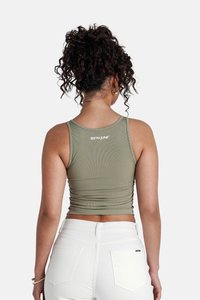 Olijfgroen geribbeld tanktop met een aansluitend ontwerp, met geplooide details op de rug en een klein wit logo bij de hals. Gecombineerd met witte jeans.