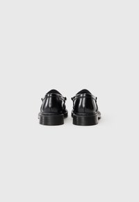 Um par de sapatos sociais de couro preto polido, mostrados de trás, sobre um fundo branco liso.