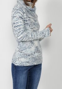 Huvtröja med mjukt, fluffigt material. Har ett blått och vitt randigt mönster med lätt glans, i kombination med tajta jeans.