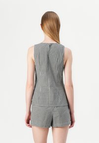 Ärmelloses Top mit schwarz-weißem Gingham-Muster, taillierten Design und kurzem Saum, mit einem Knopfverschluss am Rücken.