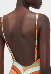 Multicolored swimsuit with orange, turquoise, and brown stripes. Features thin straps and an open back design. Textured fabric with a smooth finish.