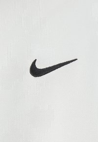 Tissu textile blanc avec une surface texturée, présentant un logo Nike brodé en noir sur le côté gauche.