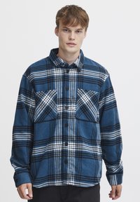 Blauw en zwart geruit shirt met een knoopsluiting aan de voorkant, kraag en twee borstzakken. Zachte textuur met duidelijke witte strepen en ruitpatronen.