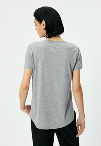 Grå T-shirt med korte ærmer og buet kantdesign, lavet af blødt stof. Enkel tekstur, bagfra ses en ren halsudskæring og minimale detaljer.